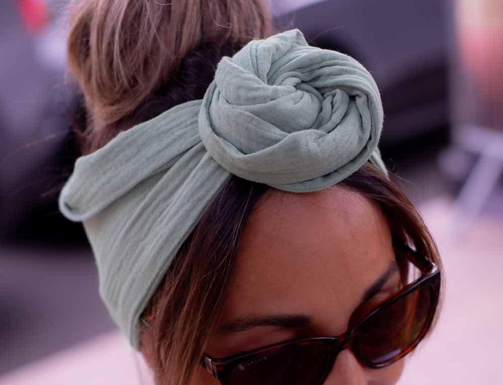 Modèle femme NDJ Occitanie portant le bandeau cheveux femme Jade noué façon rose africaine fabriqué à la main en gaze de coton Kaki.