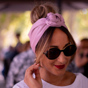 Modèle femme NDJ Occitanie portant le bandeau turban rose Livia en satin, noué façon rose africaine, fabrication artisanal.