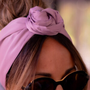 Modèle femme NDJ Occitanie portant le bandeau turban rose Livia en satin, noué façon rose africaine, fabrication artisanal.